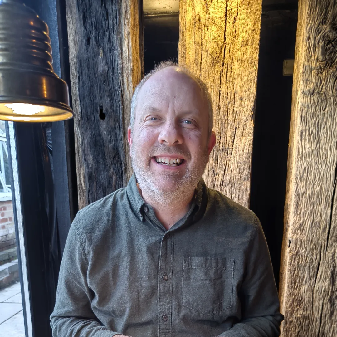 A man smiling in front of some wooden posts next to a lamp