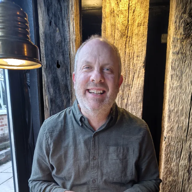 A man smiling in front of some wooden posts next to a lamp